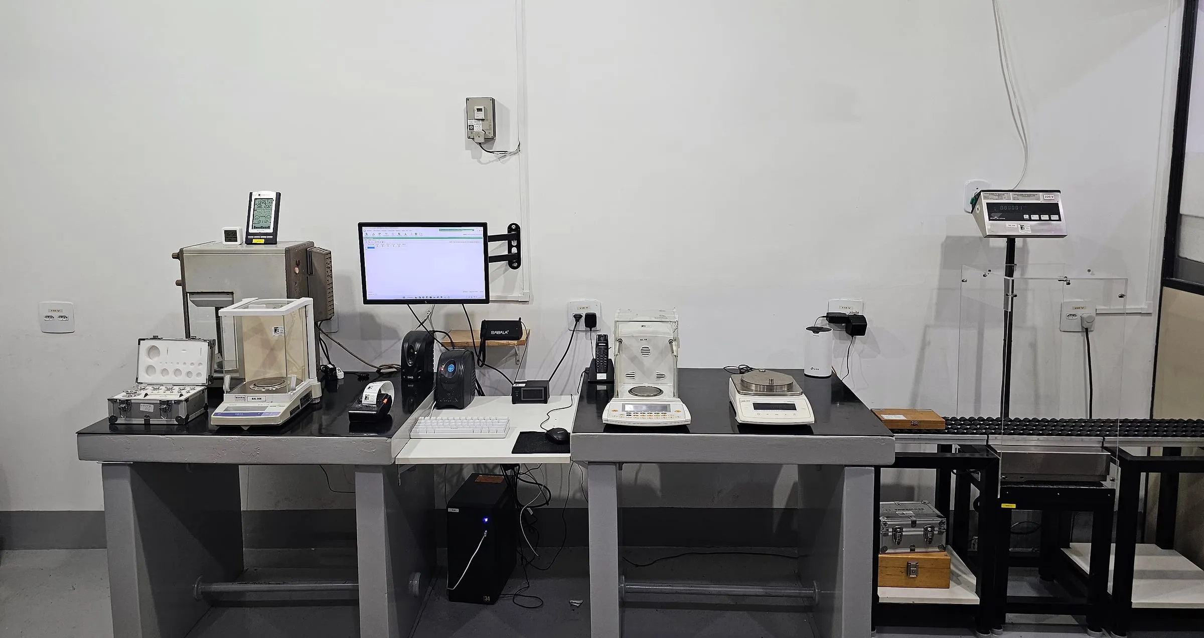 Laboratório de massa da SJS com balanças analíticas sobre bancadas de granito e comparador de massa à direita.