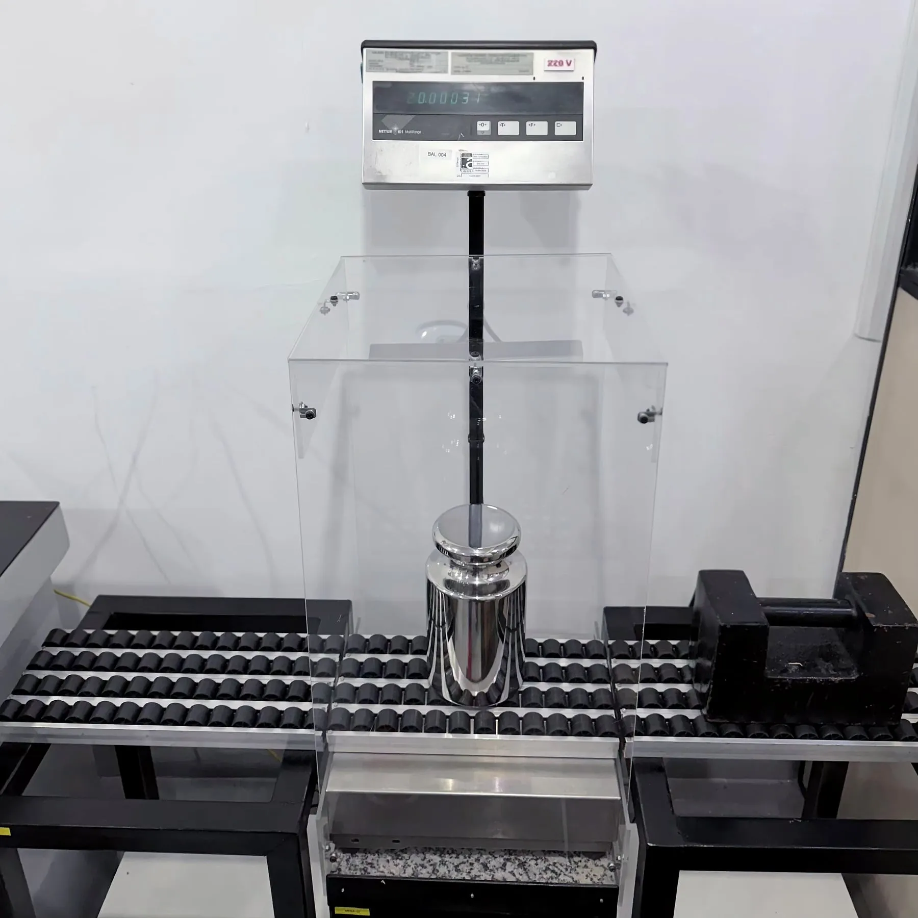 Peso-padrão de 20 kg de aço inox dentro da capela do comparador de massa