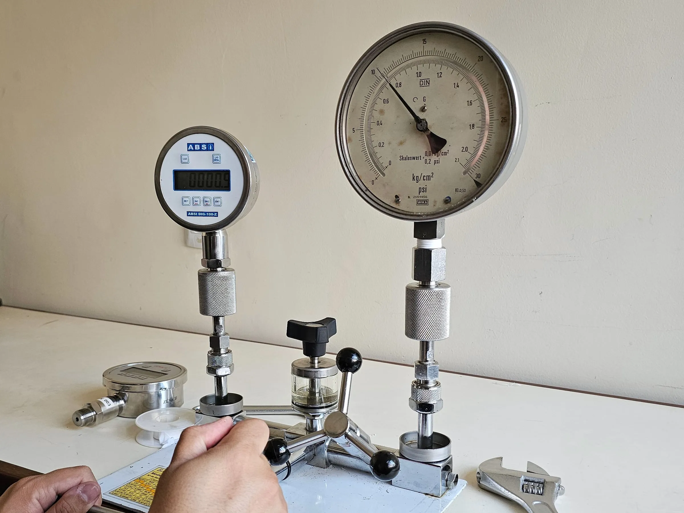 Técnico calibra um manômetro analógico comparando-o com um manômetro digital padrão na bomba de comparação