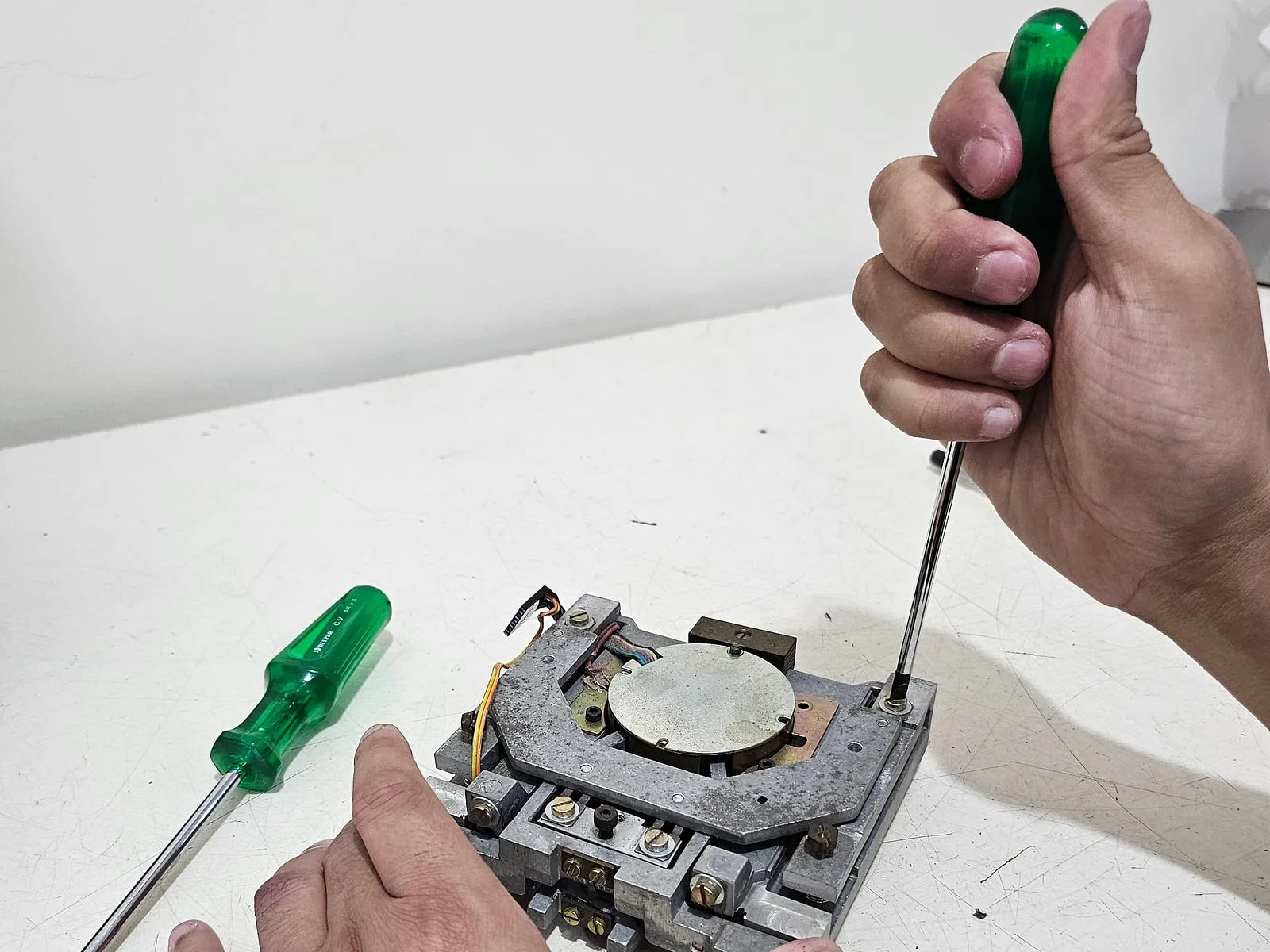 Mãos de técnico apertam com chave de fenda um parafuso do mecanismo de uma balança desmontada na oficina.