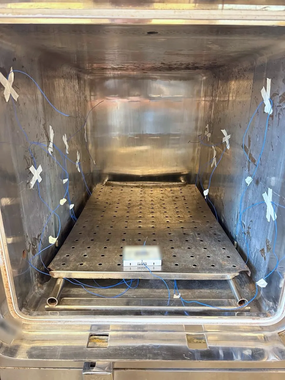 Interior da autoclave com termopares presos às paredes com fita e pacote de teste sobre a prateleira.