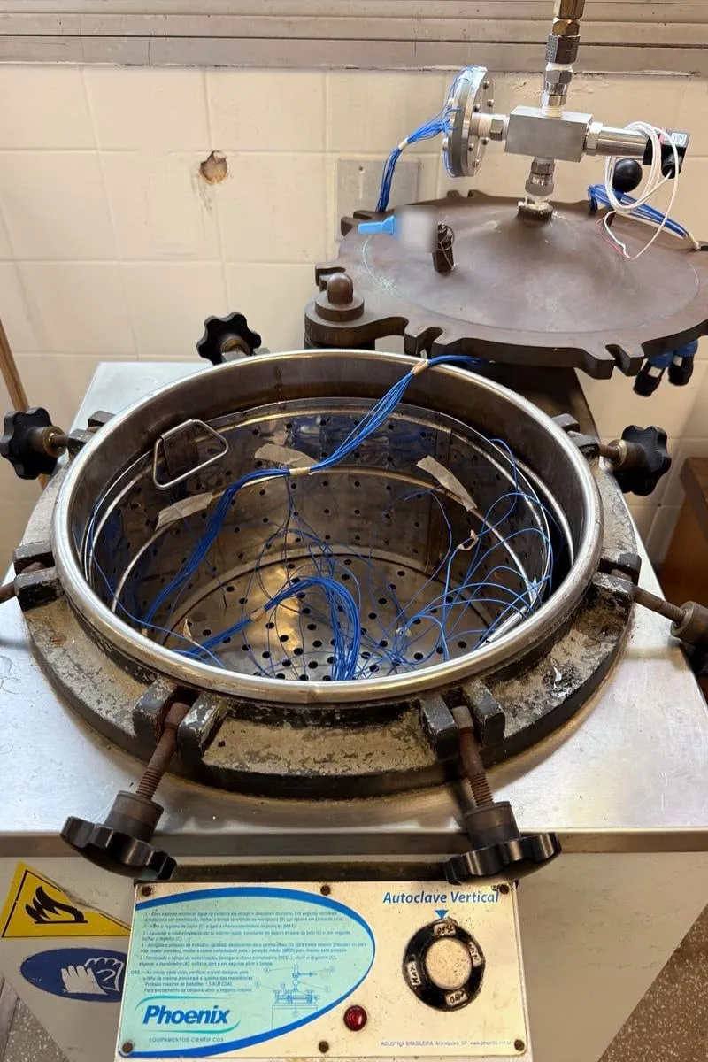Autoclave vertical com a tampa aberta e os termopares do ensaio espalhados pelo cesto.